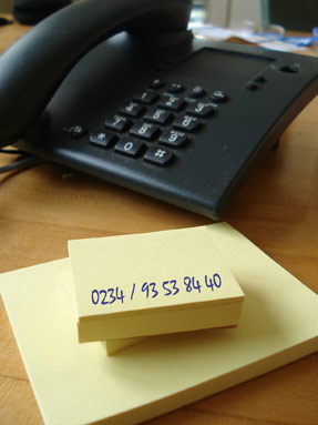 Foto eines Telefon sowie Notizblock mit Telefonnummer